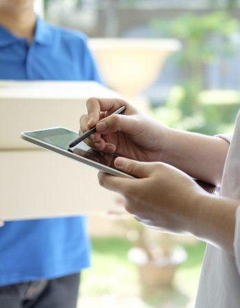 delivery, mail, people and shipping concept.Young woman sign in digital mobile phone after receiving parcel from courier at home.